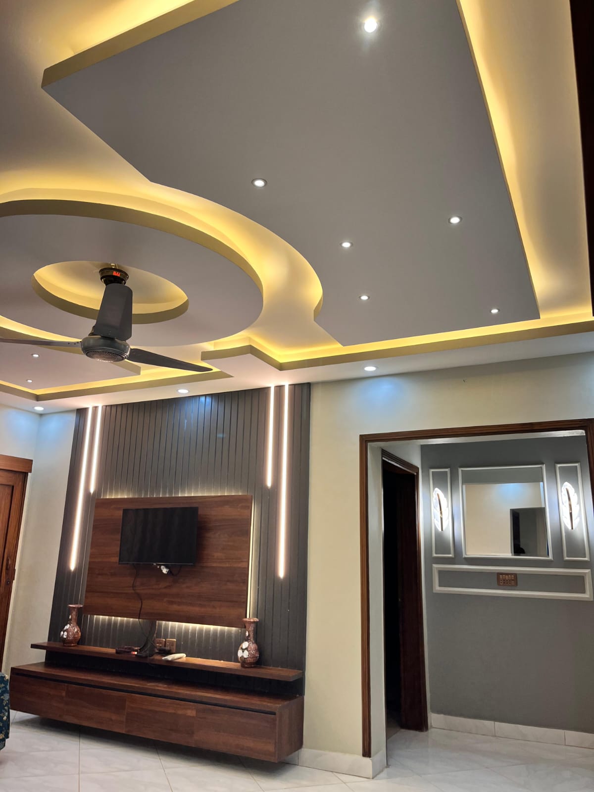 Modern living room with gypsum false ceiling and TV media wall completed by Etminaan Services.